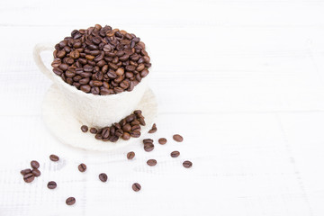 cup full of coffee beans on a white wooden background