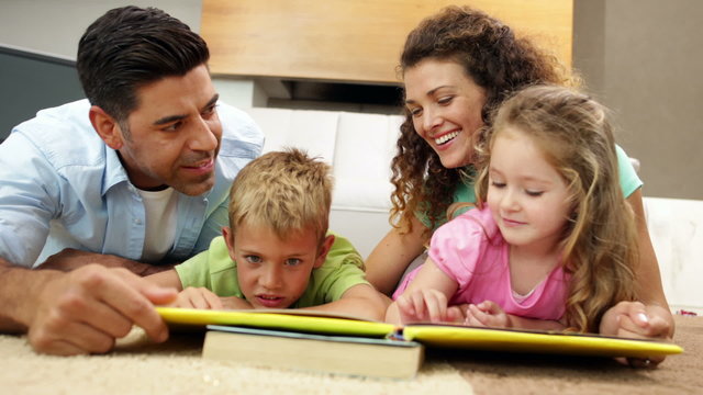 Siblings lying on floor reading book with parents
