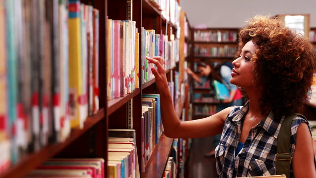 Pretty student picking out a book in library