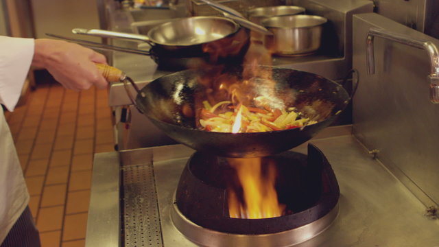 Chef tossing stir fry over large flame