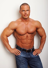 Handsome muscular standing man poses at the wall