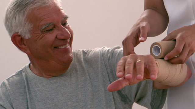 Physiotherapist bandaging elderly mans arm