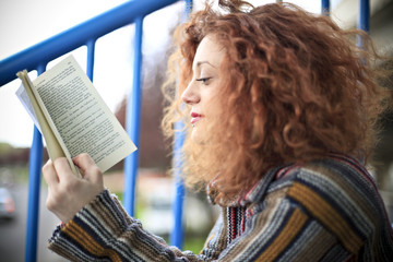 Beautiful girl reading a book on a balcony