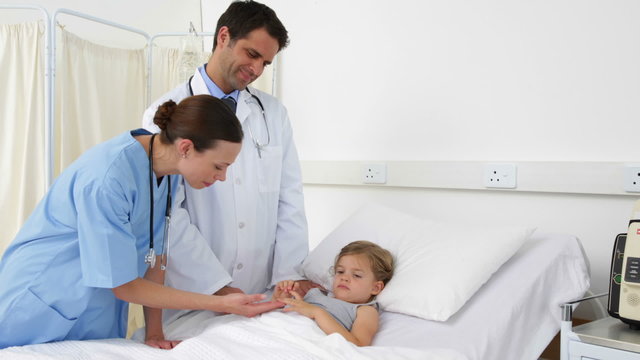 Sick little girl lying in bed talking to nurse and doctor