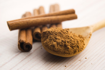 Cinnamon, whole sticks behind wooden spoon with a heap of powder