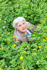 Happy beautiful elderly woman sitting on a glade of yellow flowe