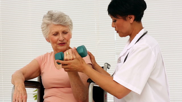 Nurse talking with patient in a wheelchair lifting a dumbbell