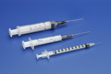 Three plastic disposable syringes with a needle on blue backgrou