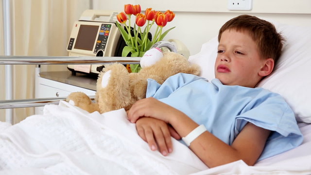 Little sick boy lying in bed with teddy bear