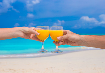 Two hands hold glasses with orange juice background blue sky