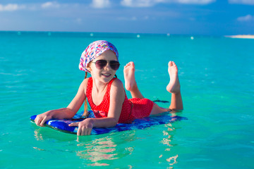 Little girl swimming on a surfboard in the turquoise sea