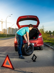 man changing punctured wheel on broken car