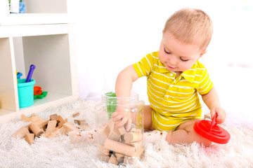 Cute little boy with wooden toy blocks in room