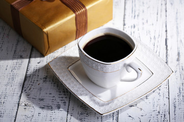 Cup of coffee and gift on wooden table close-up