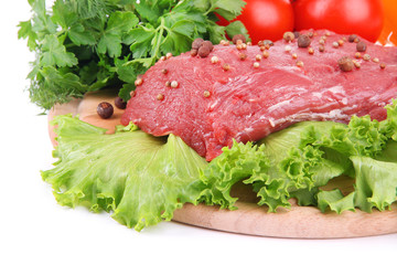 Raw beef meat with vegetables on wooden cutting board close up