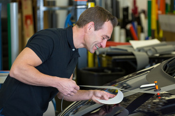 Worker in car wrapping workshop glues foil to car
