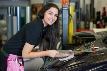Worker in car wrapping workshop glues foil to car