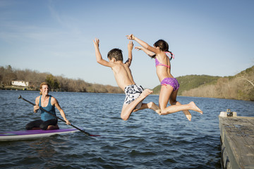 Two children leaping into the water from a jetty.