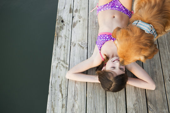 A young girl and a golden retriever dog on a jetty.