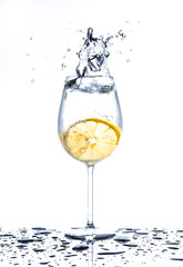 Lemon splashing into glass of water on white background