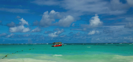 Red boat on azure water among exotic palm trees