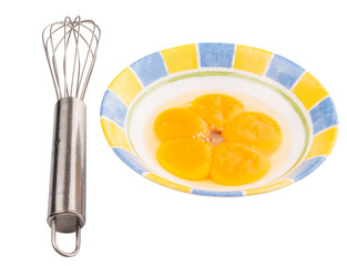 An egg beater with egg yolk in a ceramic bowl