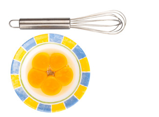 An egg beater with egg yolk in a ceramic bowl