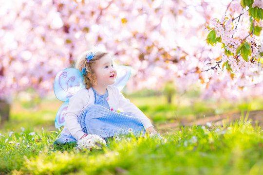 Curly Toddler Girl In Fairy Costume Walking In Fruit Garden