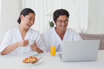 Fototapeta na wymiar Happy couple using laptop over breakfast