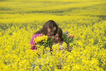 Fototapeta premium Girls holding Spring flowers in rapeseed field