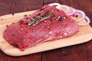 Raw beef meat with spices on cutting board on wooden background