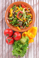 Beef salad on plate with vegetables on wooden background