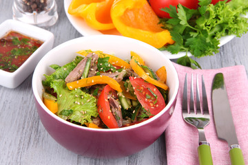 Beef salad in bowl with vegetables and spices on wooden table