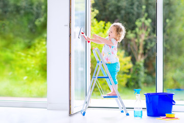 Little girl washing a window with view garden