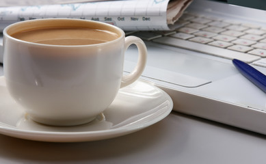 cup of coffee near the laptop and newspapers.