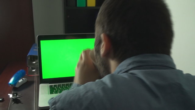Man Browsing Trough Laptop WIth Green Screen, Back Shot