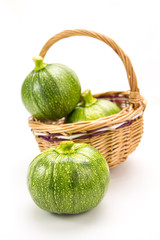Three round zucchinis in wicker basket isolated on white
