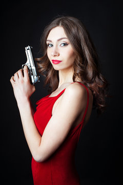 Beautiful young woman in red dress holding gun