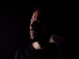 Low key image of a bearded man with a sore neck