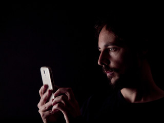 Low key image of a bearded man with a cellphone
