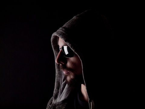 Low key image of a bearded man with a hoody and sunglasses