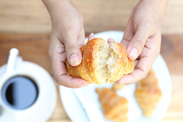 a woman hand with a cup of black coffee and a freshly baked cro