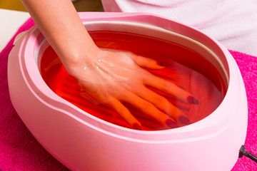 Female hand and orange paraffin wax in bowl.    - obrazy, fototapety, plakaty