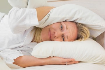 Obraz na płótnie Canvas Irritated woman covering ears with pillows