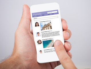 Hand Holding Smartphone With Social Site Displayed On Screen