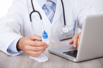 Doctor Holding Drop Bottle While Using Laptop