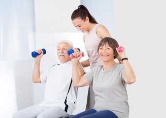 Trainer Assisting Senior Couple With Dumbbells