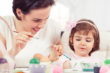 Obraz na płótnie Canvas Cute little girl painting Easter eggs with mommy.