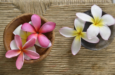 Fototapeta na wymiar White and pink frangipani in water bowl on Brown straw mat