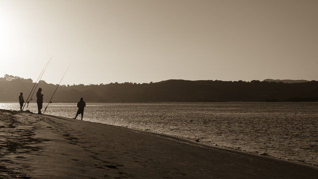Fishermen in sepia silhouette at beach at dawn.